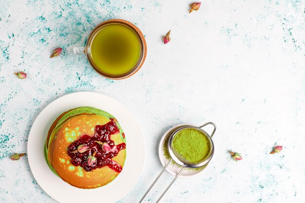 Green pancakes with matcha powder with red jam, top view