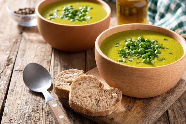 素朴な木製テーブルのボウルにグリーンエンドウ豆のスープ