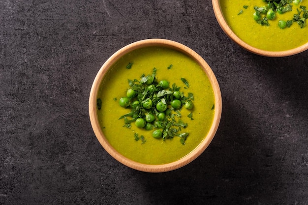 Green pea soup in a wooden bowl on black background