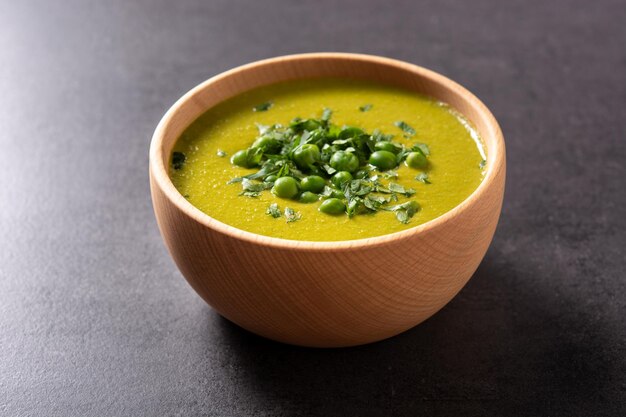 Green pea soup in a wooden bowl on black background