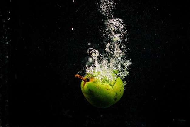 Green pear splashes water falling on black background