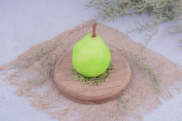 A green pear on a wooden board with pumpkin seeds