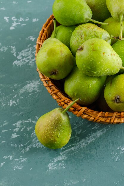 Green pears in a basket on plaster surface