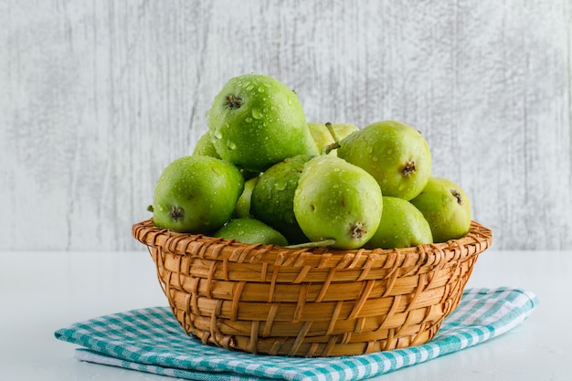 Green pears with kitchen towel in a basket on white and grungy.