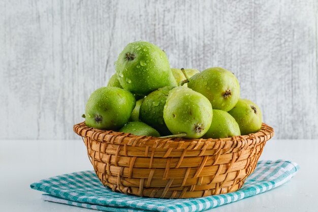 Green pears with kitchen towel in a basket on white and grungy.