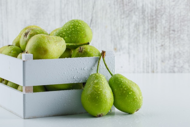 Green pears in a wooden box on white and grungy background, side view.