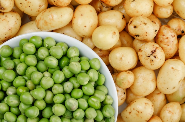 Green peas in a white bowl on potatoes wall, close-up.