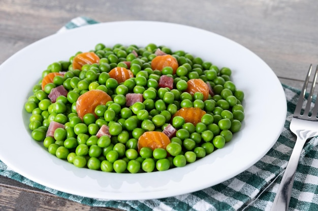 Green peas with serrano ham and carrot on wooden table