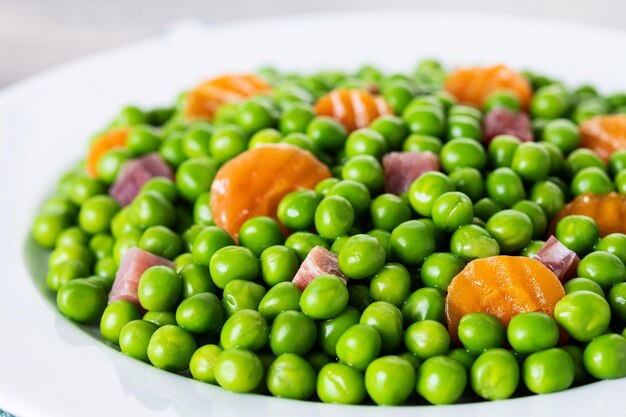 Green peas with serrano ham and carrot on wooden table