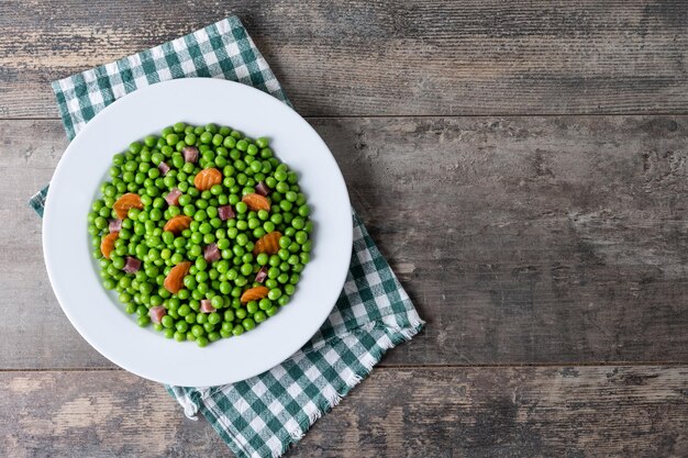 Green peas with serrano ham and carrot on wooden table