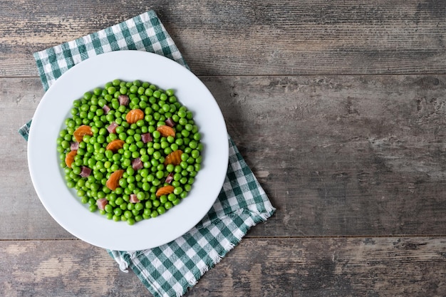 Green peas with serrano ham and carrot on wooden table