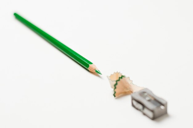 Зеленый карандаш и точилка на белом фоне