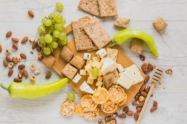 Green peppers, grapes, dried fruits, crackers, crisp bread and cheese blocks on wooden desk