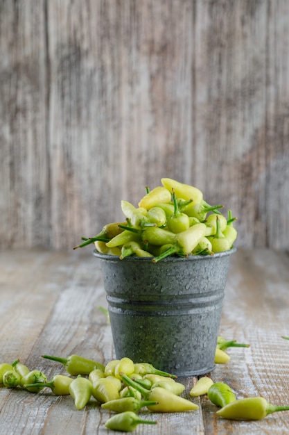 Free photo green peppers in a mini bucket side view on a wooden