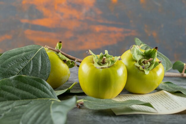 Green persimmons with leaves and book page on marble table