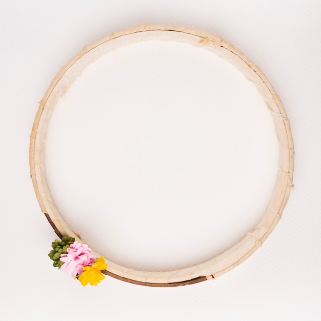 Free photo green; pink and yellow flowers on wooden circular frame against white backdrop