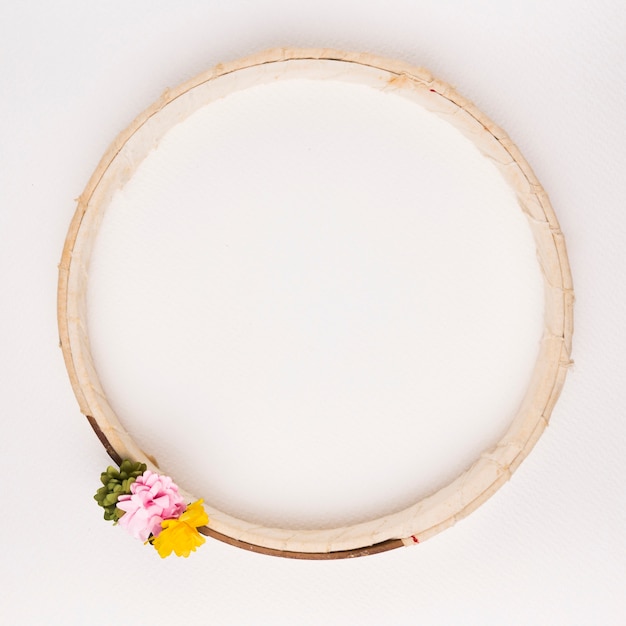 Green; pink and yellow flowers on wooden circular frame against white backdrop