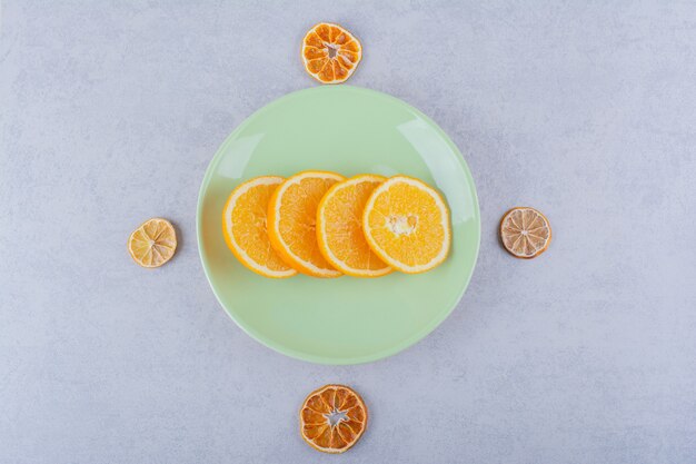 Green plate of fresh orange slices on stone.