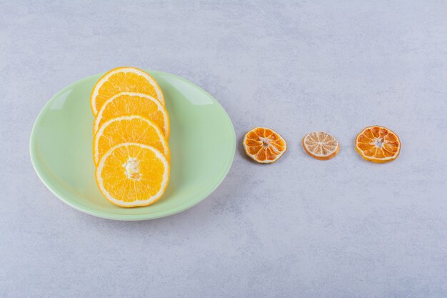 Green plate of fresh orange slices on stone.