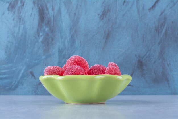 Зеленая тарелка, полная красных сладких мармеладных конфет на сером фоне. Фото высокого качества