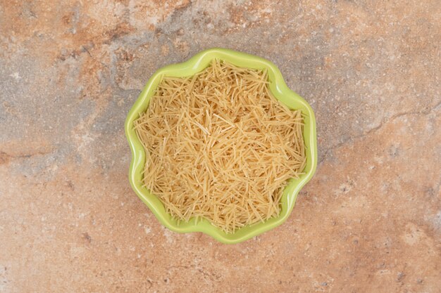 A green plate full of small vermicelli on marble background. High quality photo