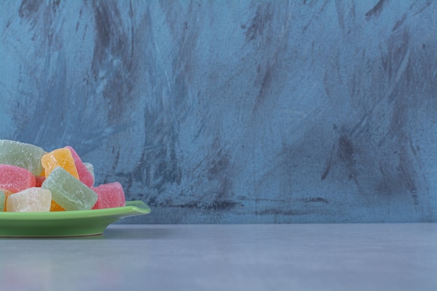 A green plate full of sugary jelly candies on gray surface 