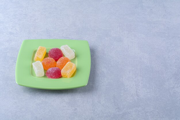 A green plate full of sugary jelly candies on gray surface