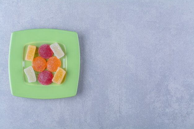 A green plate full of sugary jelly candies on gray surface