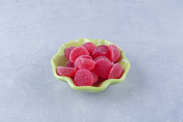 A green plate full of sugary jelly candies on gray table . 