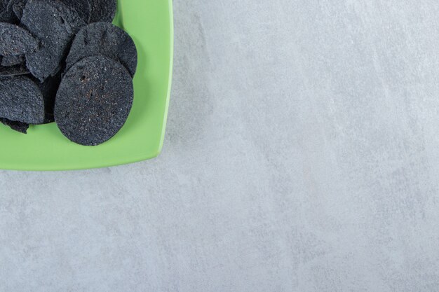 Бесплатное фото Зеленая тарелка соленых хрустящих черных чипсов на камне.