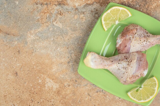 A green plate of uncooked chicken legs with sliced lemon