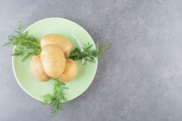 A green plate of uncooked potatoes with fresh dill . 