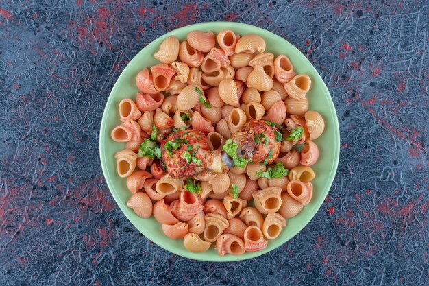 Зеленая тарелка с жареными куриными ножками с макаронами.