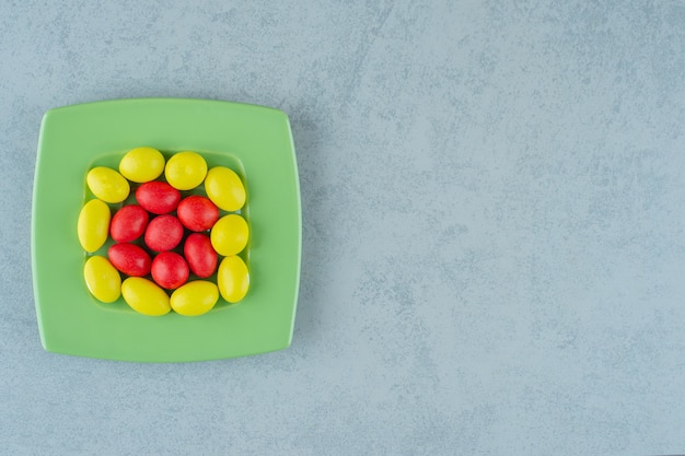 A green plate with sweet yellow and red candies on white surface