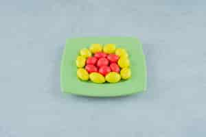 Foto gratuita un piatto verde con dolci caramelle gialle e rosse su superficie bianca