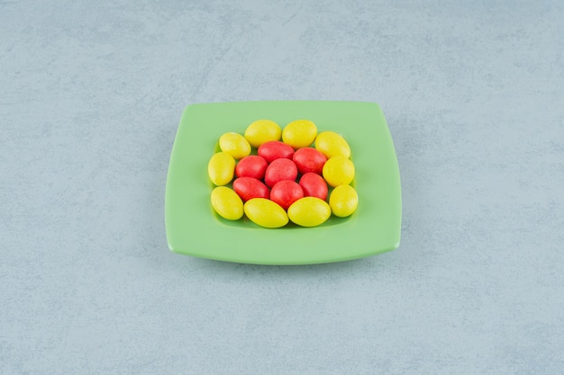 Зеленая тарелка со сладкими желтыми и красными конфетами на белой поверхности