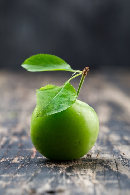 Green plum with leaves on wooden and grungy wall, side view.