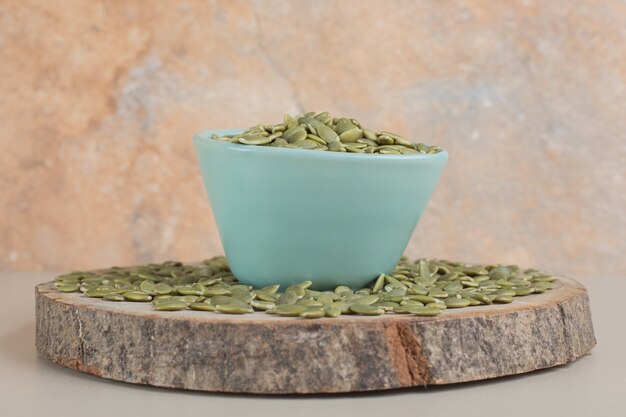 Green pumpkin seeds in a container on concrete.