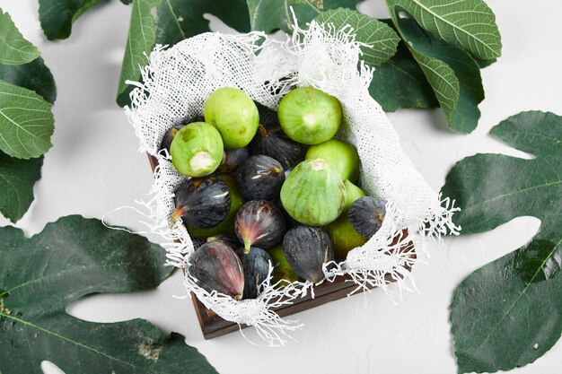 Green and purple figs in a wooden tray on the towel. 