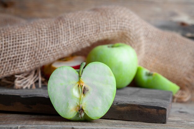 Green and red apples cut in a half on a wood, cloth and dark wooden background. side view.