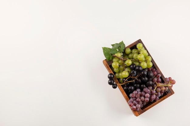 Green and red grape bunches in a wooden box in the bottom side