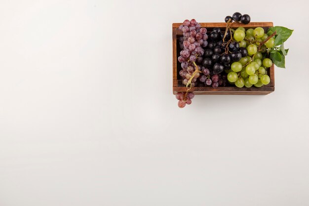 Green and red grape bunches in a wooden box in the corner