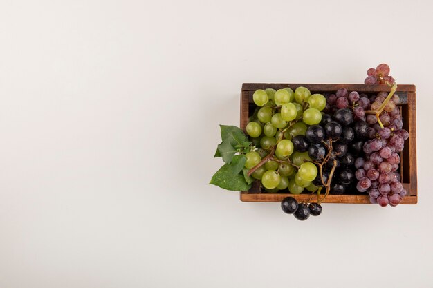 Green and red grape bunches in a wooden box isolated oin white