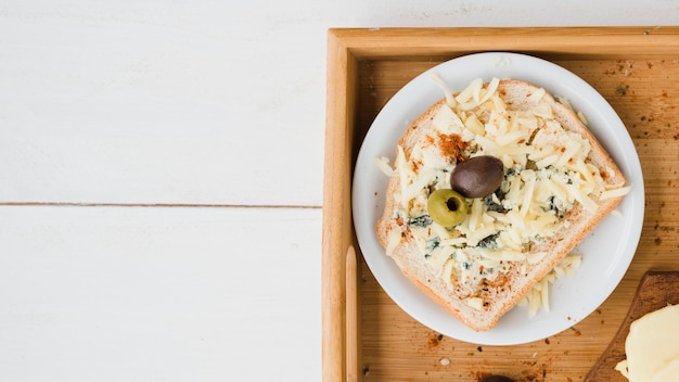 Зеленые и красные оливки с тертым сыром на хлебе над тарелкой в лотке