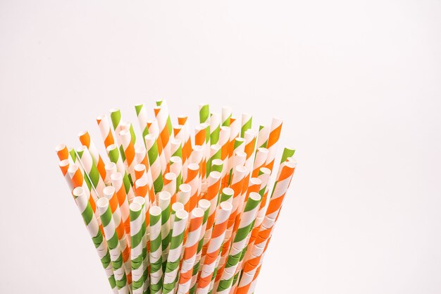 Green, red and white striped drinking tubes in a glass isolated on a white wall