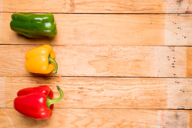 Green; red and yellow bell peppers on wooden plank