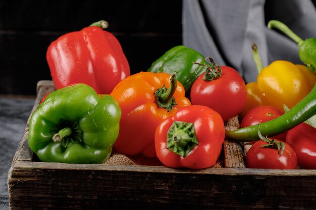 Green, red and yellow bell peppers in a wooden tray.