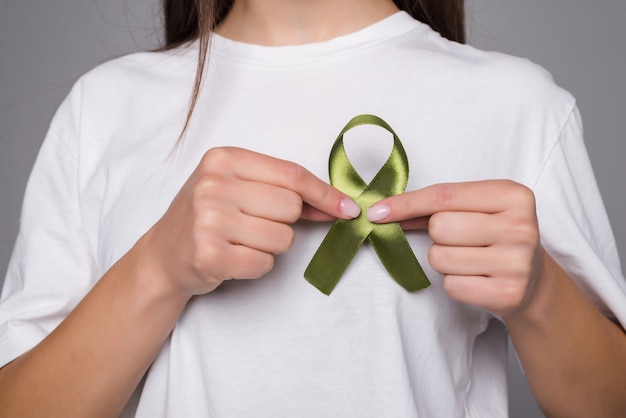 Free photo green ribbon a symbol of kidney cancer isolated on gray wall