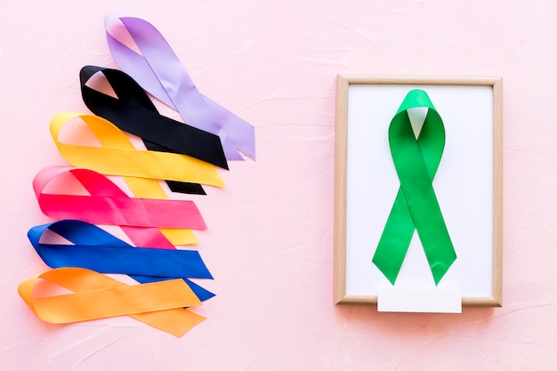 Green ribbon on white wooden frame near the row of colorful awareness ribbon