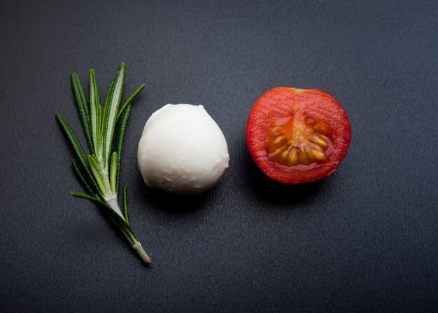 Green rosemary; half cheery tomato and mozzarella cheese over black surface